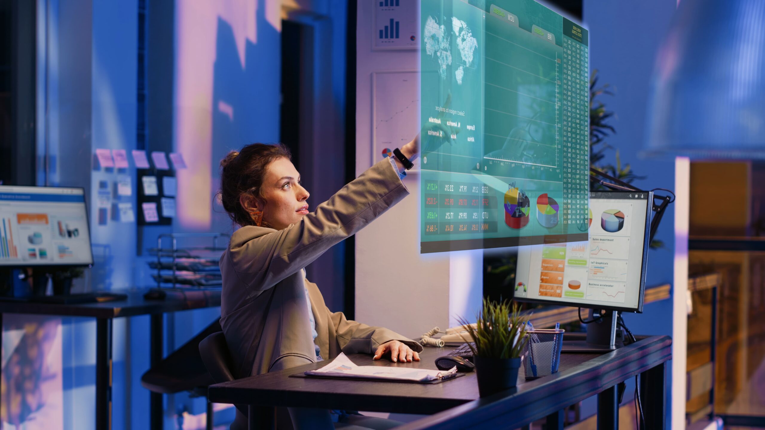 Mulher sentada à secretária a tocar em imagem holográfica projetada com gráficos