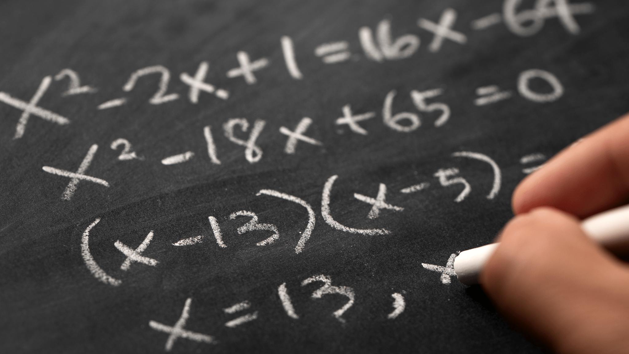 Hand with chalk writing equations on a slate