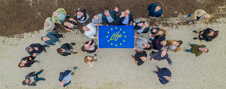 fotografia de drone com pessoas a acenar, segurando numa bandeira do projeto Life