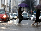 Foto de peões a atravessar passadeira com a rua parcialmente inundade.