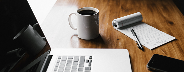 mesa com computador, caneca de café e bloco de notas