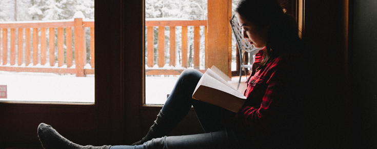 Jovem a ler um livro perto de uma janela