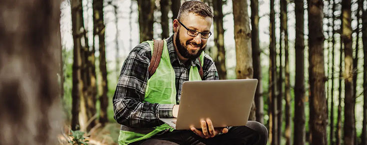 Fotografia de homem a utilizar um computador portátil no meio de uma floresta